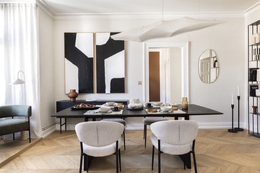 Salle à manger avec table noire sculpturale, chaises bouclées et grande œuvre graphique noir et blanc